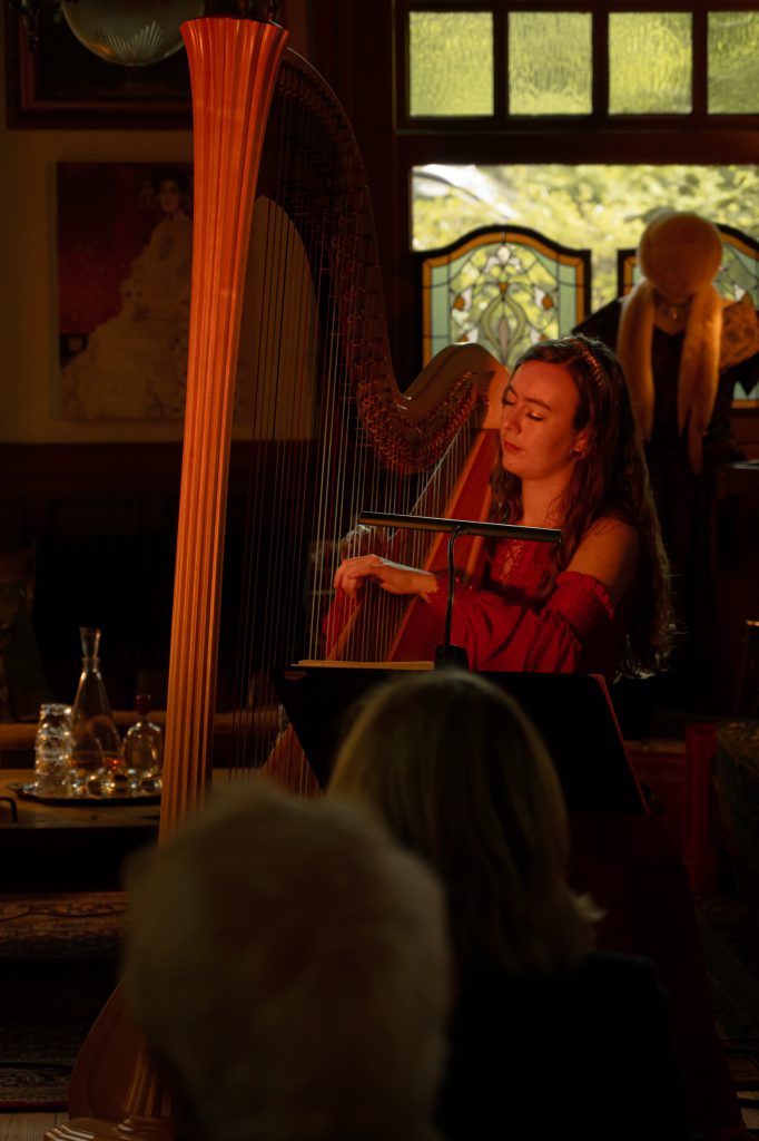 The harpist in red playing her golden harp beneath stained-glass windows