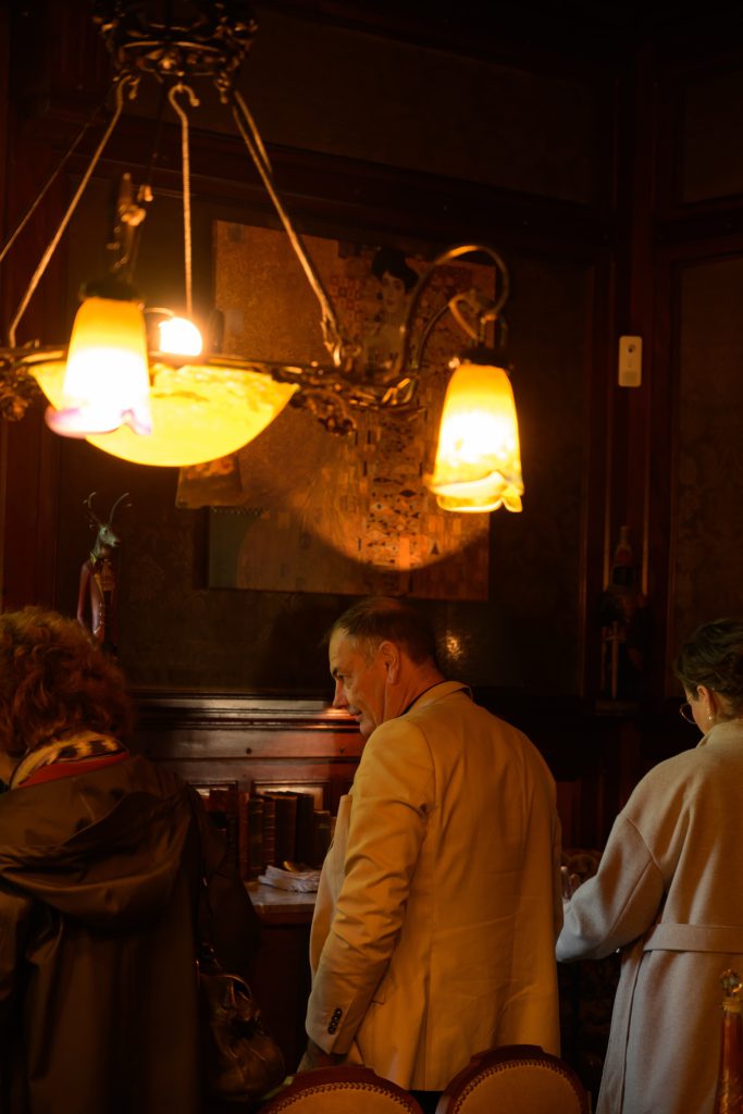 Guests entering a wood-panelled hall under a lit art-nouveau chandelier