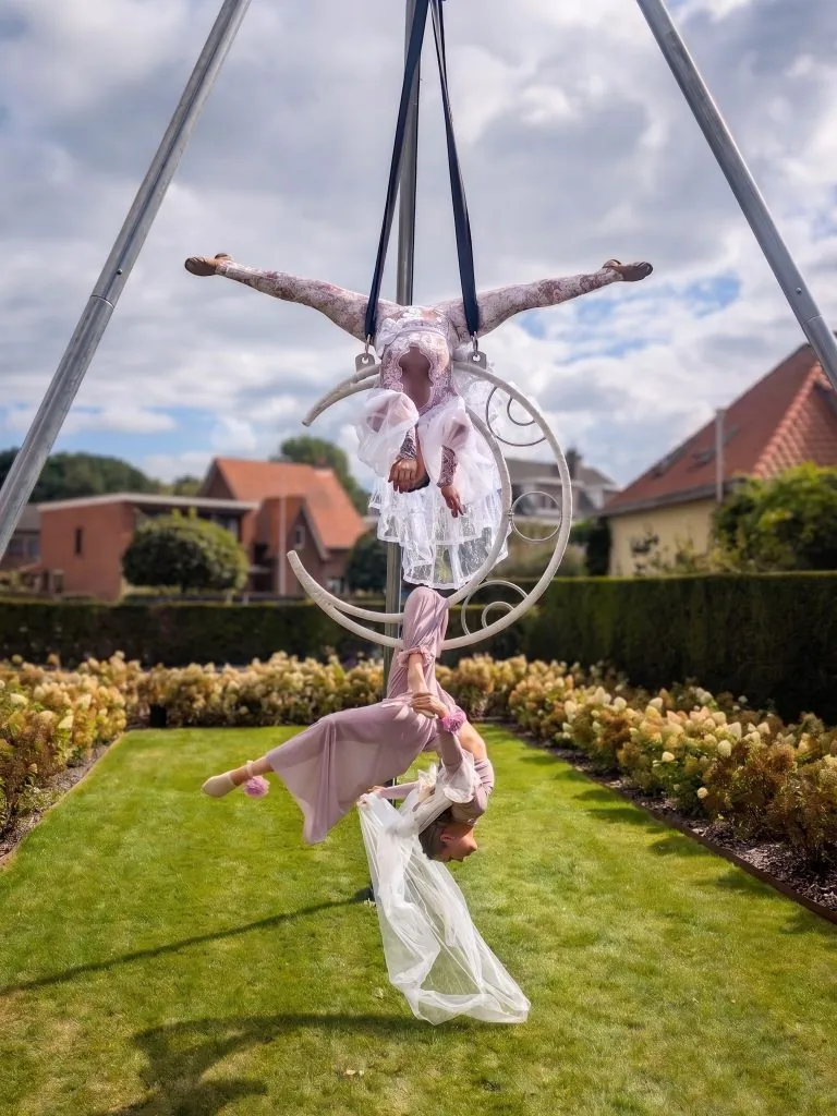 Two aerial acrobats in lilac costumes performing on an aerial hoop in a garden