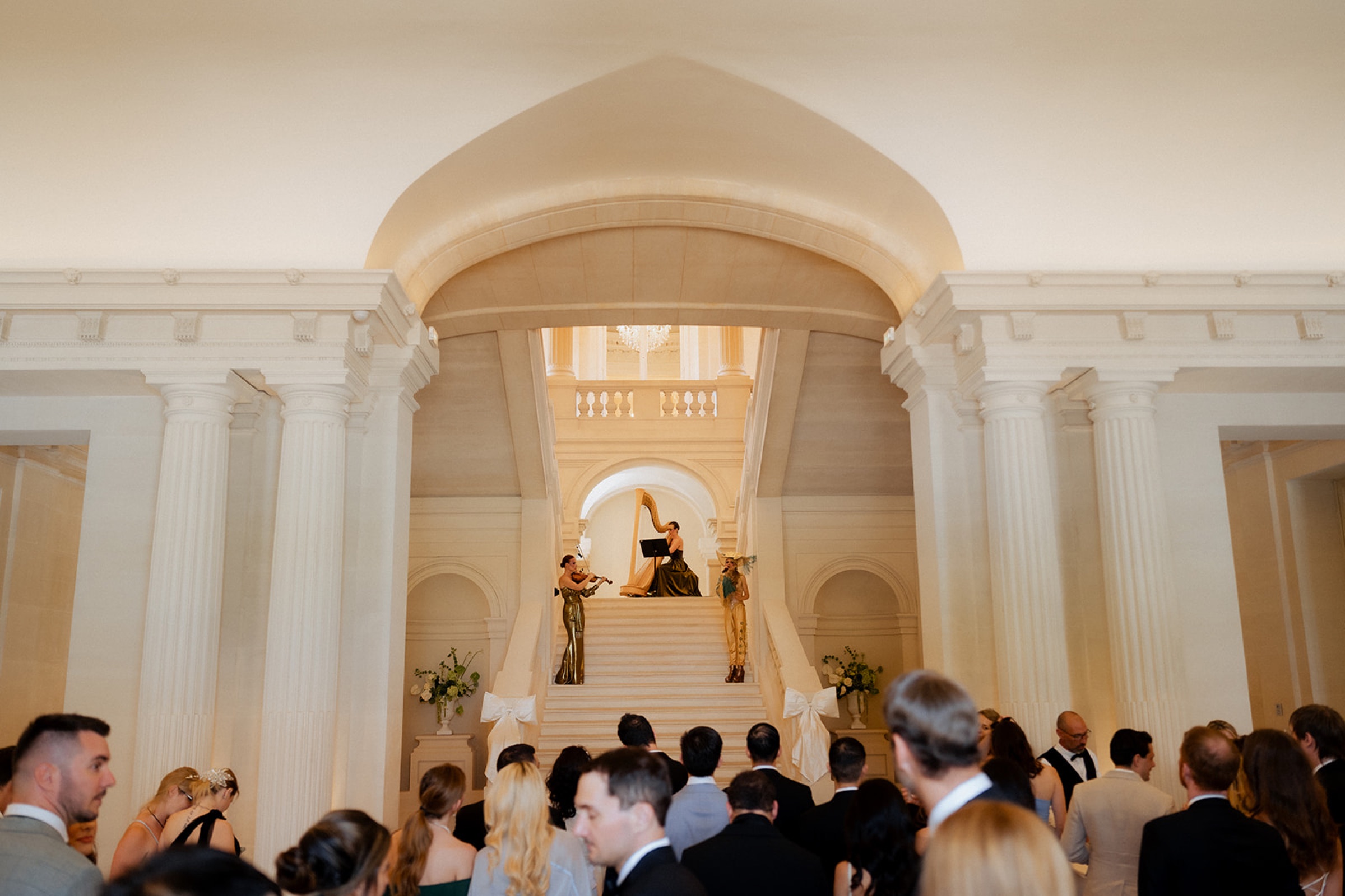 Guests watching a harpist and a singer perform on a grand marble staircase