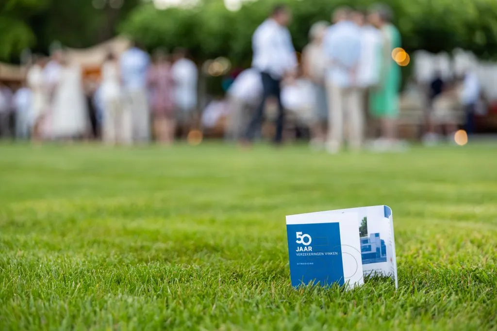 A Verzekeringen Vinken 50-year card on the lawn, guests gathering in the garden behind it