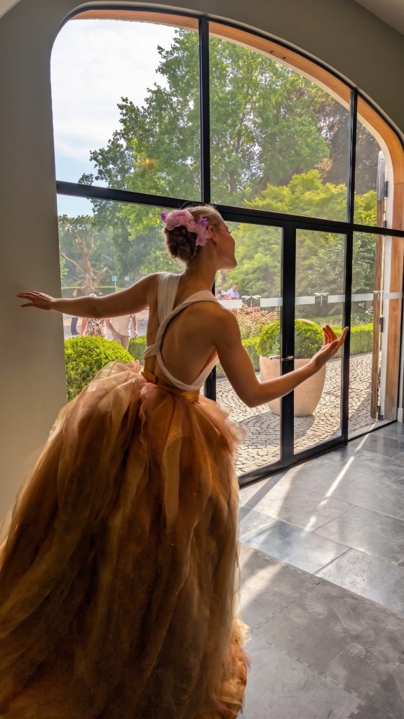 The swayball dancer in a golden gown welcoming guests at a tall arched window