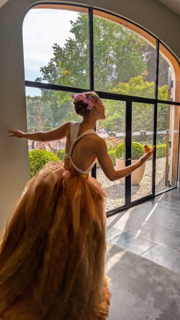The swayball dancer in a golden gown welcoming guests at a tall arched window