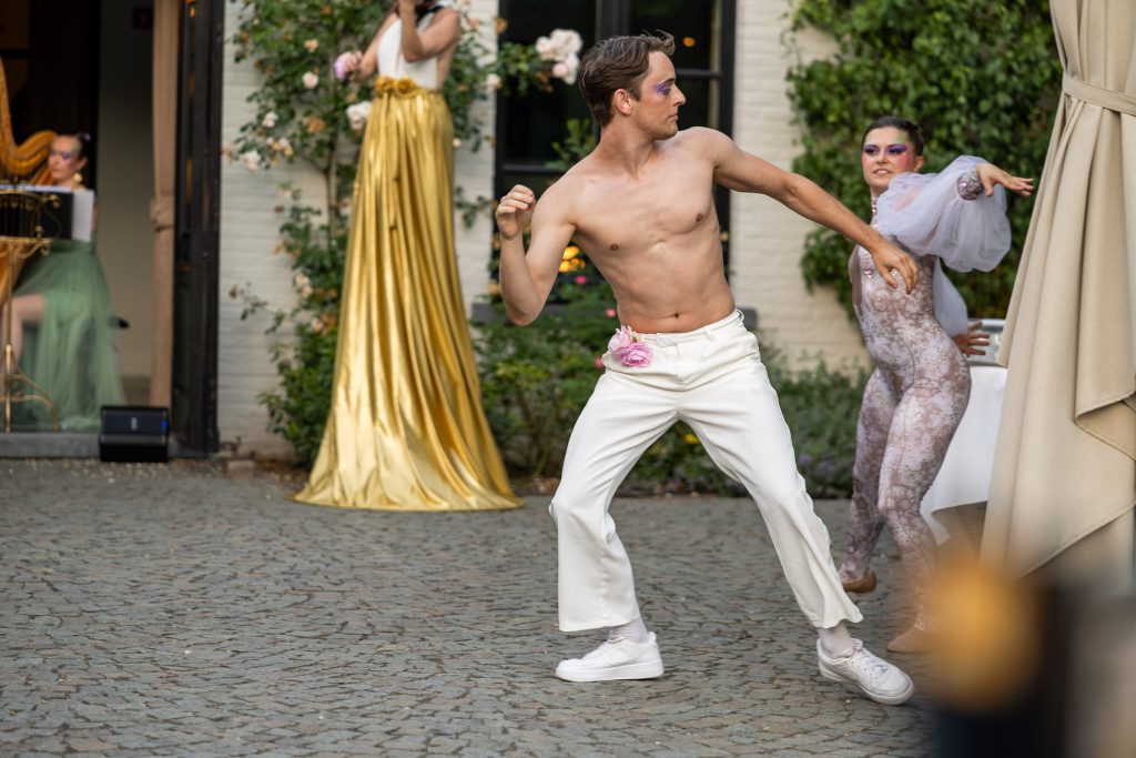 A dancer mid-move on the cobbled courtyard, musicians in gold behind him