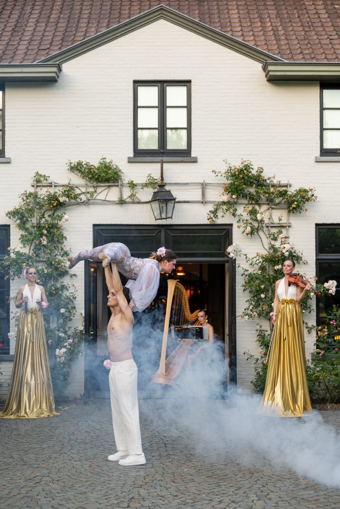 The grand finale: an acrobatic lift in stage smoke, flanked by a harpist and violinist in gold