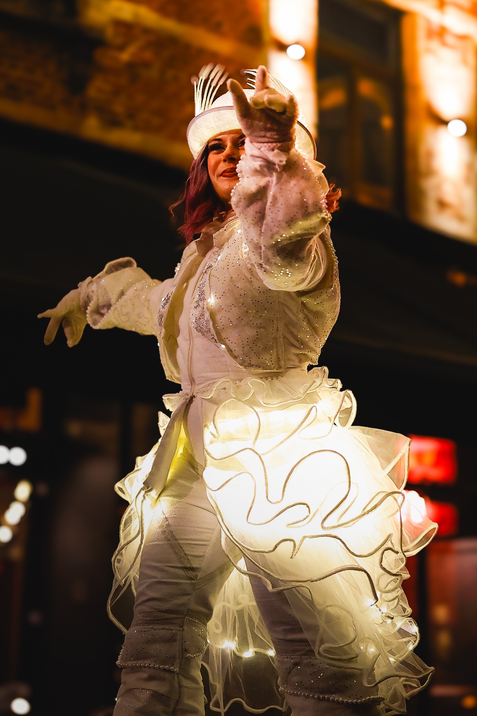 Lady of the Light in her glowing costume, one arm stretched out in a night-time street