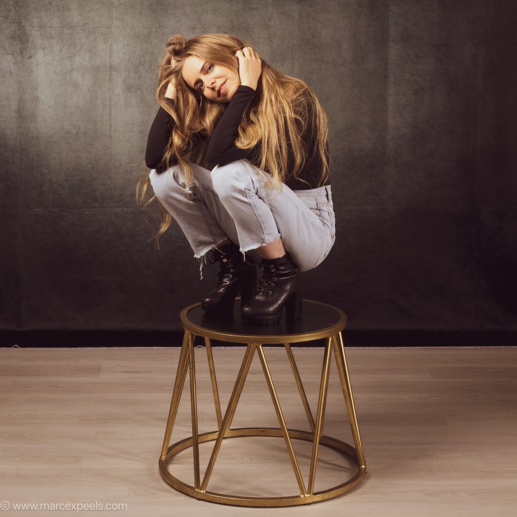Liza Dedapper crouching on a golden stool in a studio, hands in her hair