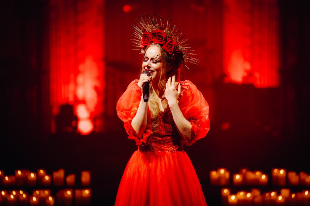 Liza Dedapper singing in a red gown and a spiky red crown, surrounded by candlelight