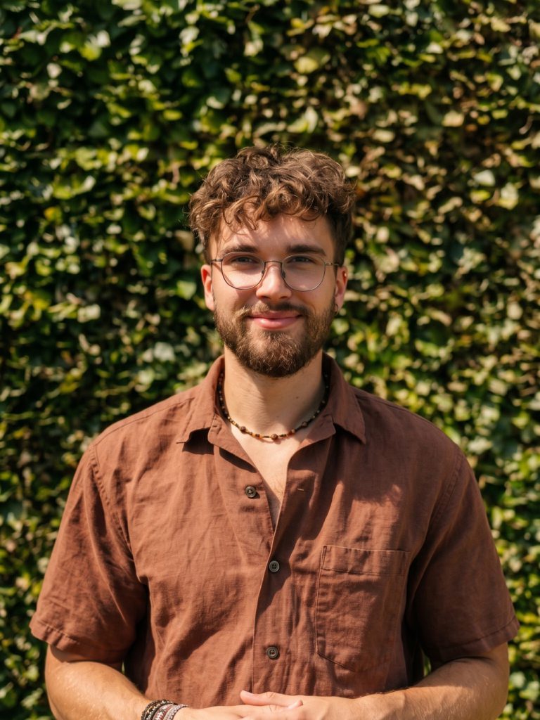 Louka Stouten smiling in front of a green hedge