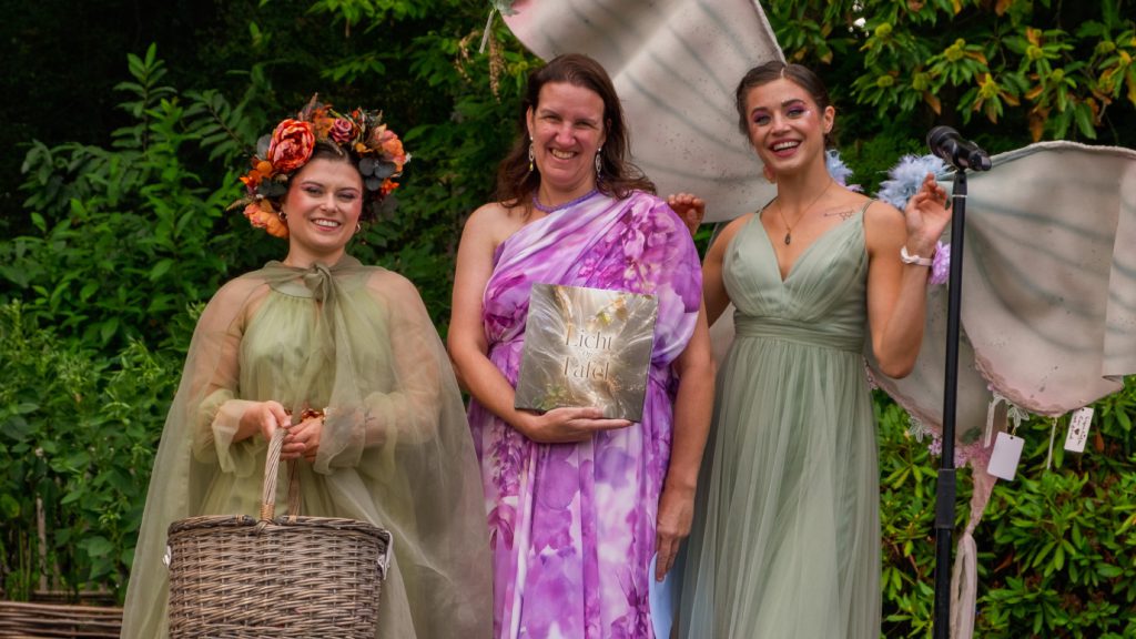 Wendy Van Looy holding her book between two elves in the garden at Villa Tulsi
