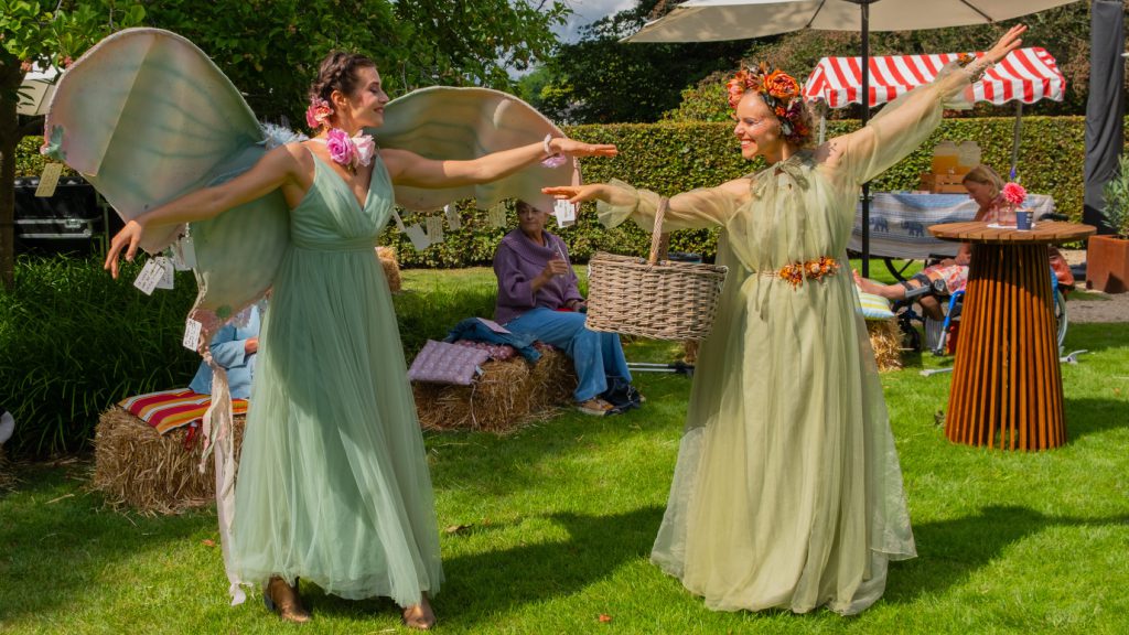 Two elves with wings and a basket dancing on the lawn among the guests