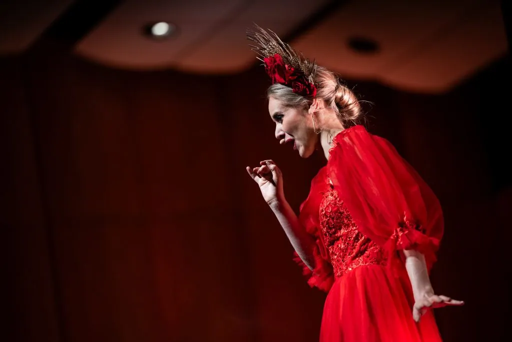 A singer in a red gown and feathered headpiece performing on stage