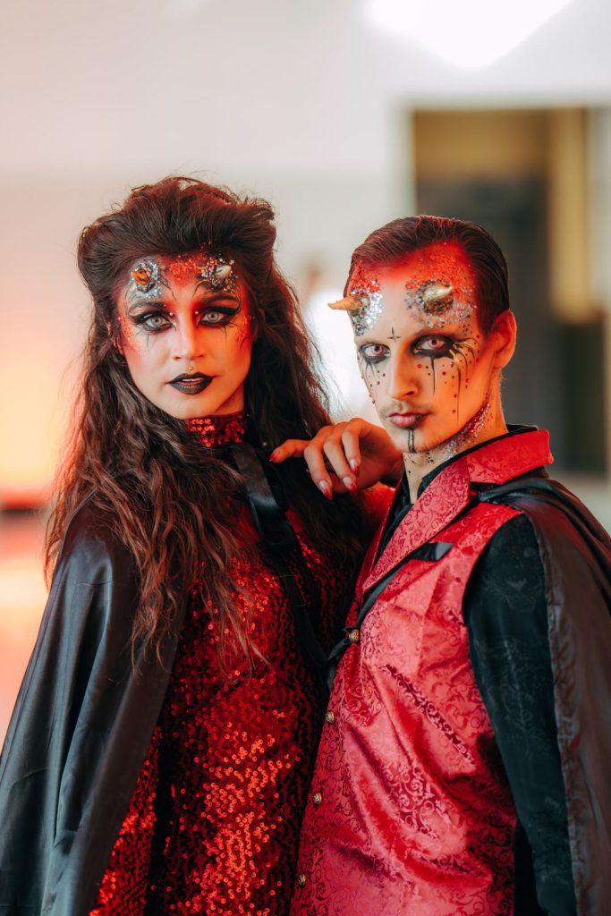 A duo in intricate red and black stage make-up, photographed close up in warm light