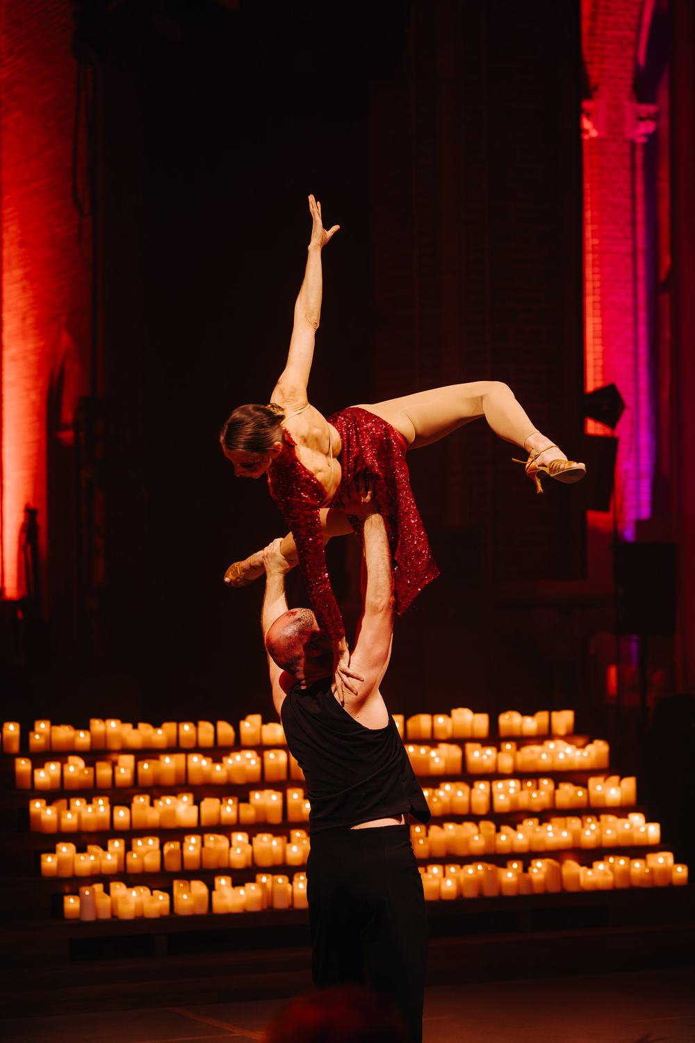 An acrobatic lift in front of a wall of candlelight inside a historic church