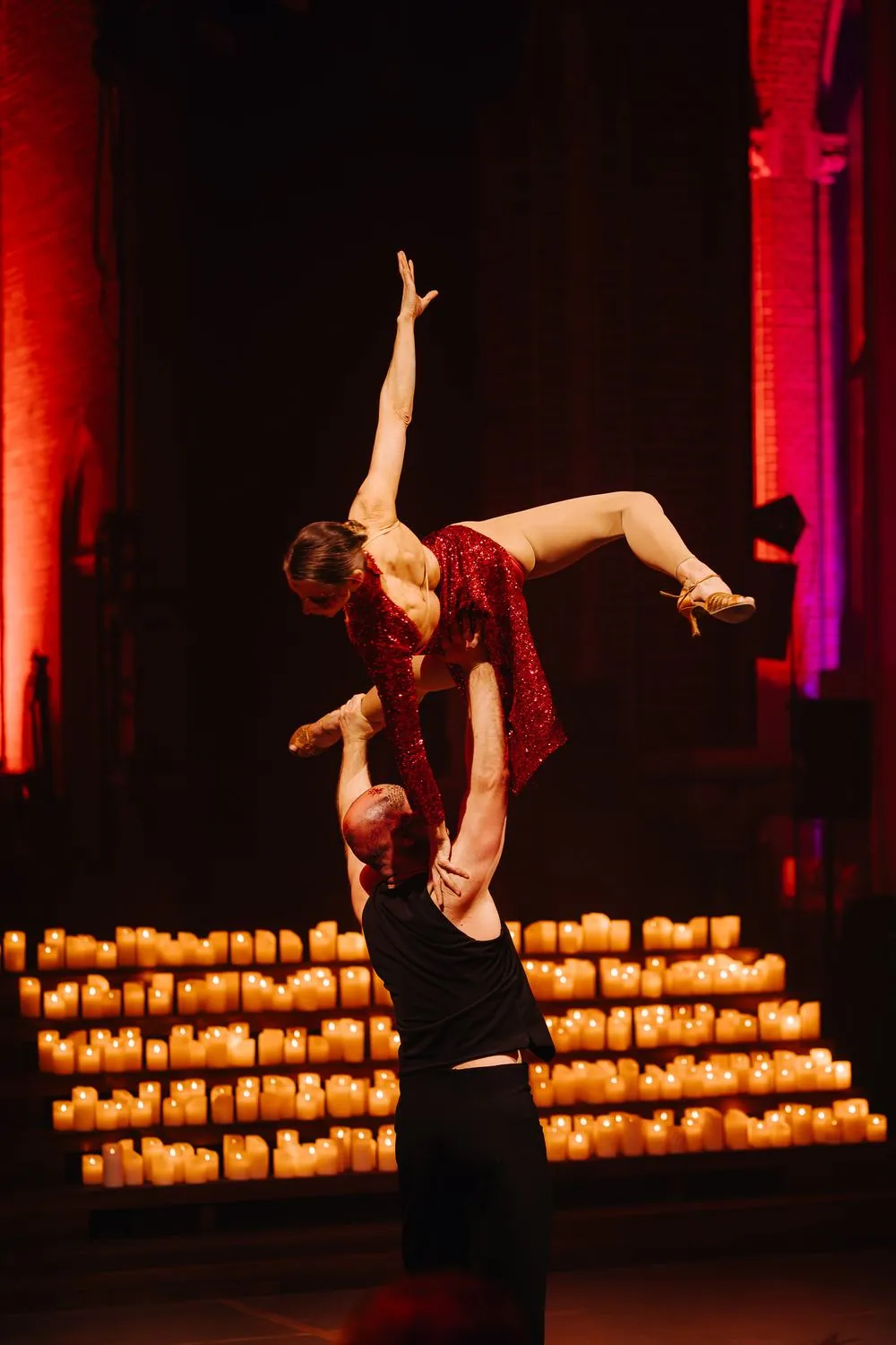 An acrobatic lift in front of a wall of candlelight inside a historic church
